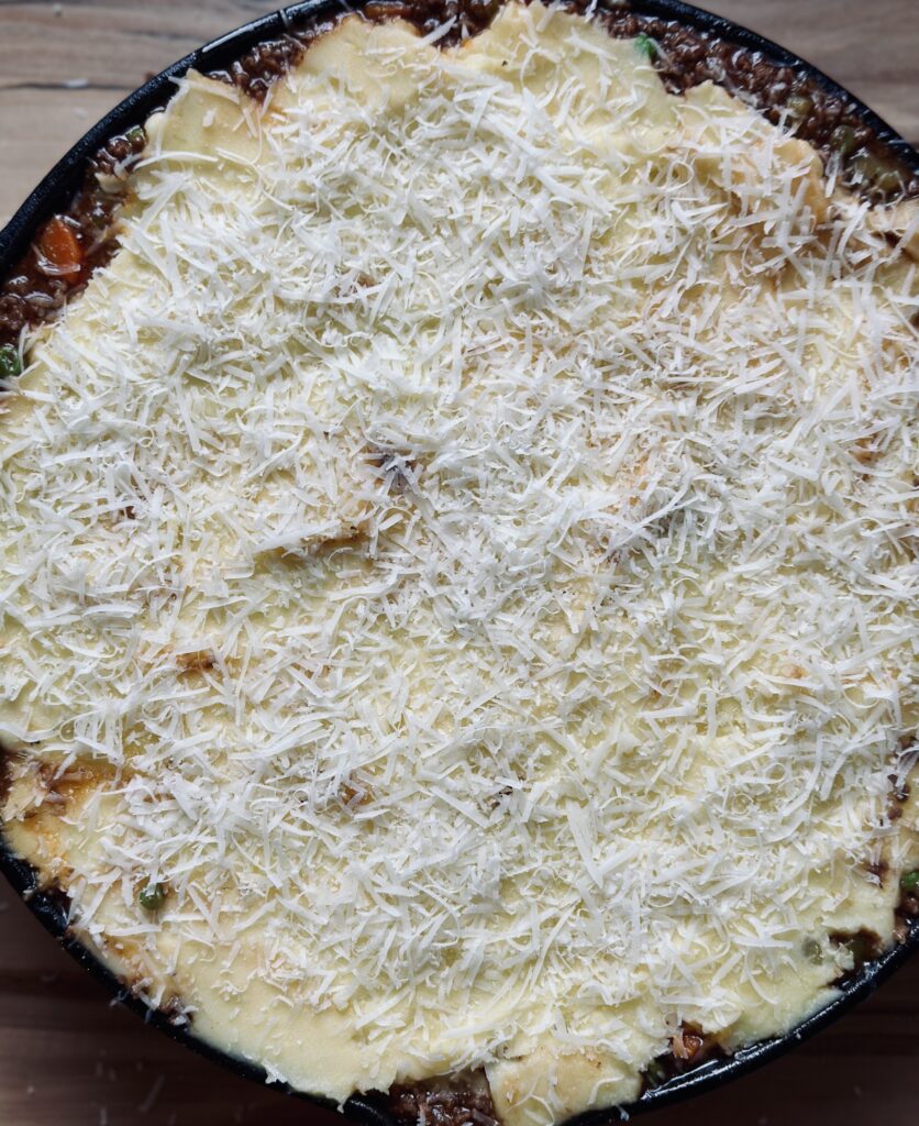 Parmesan über dem Shepherd's Pie verteilen